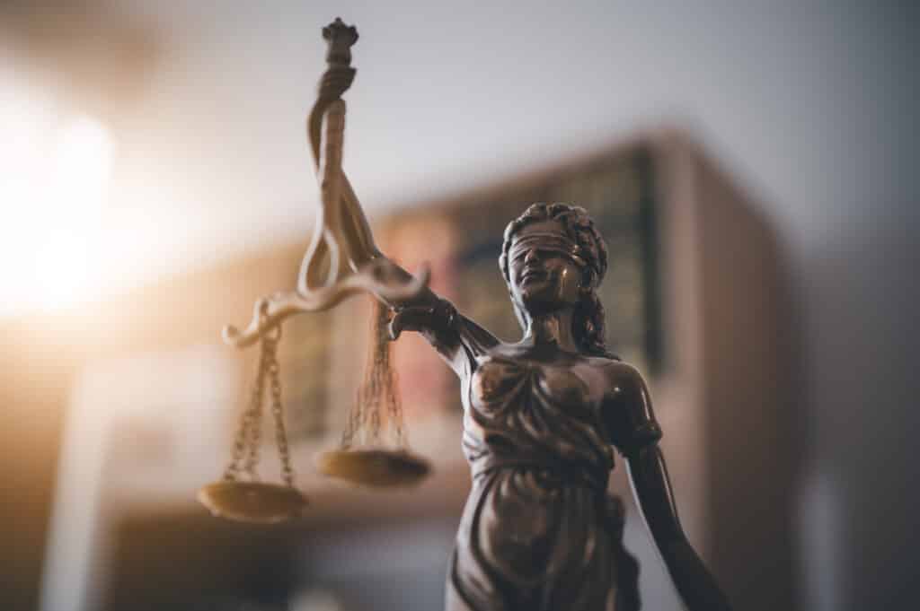 Bronzeskulptur der Justitia, die mit verbundenen Augen eine Waage hält. Symbolisiert Gerechtigkeit und Fairness im Rechtssystem.