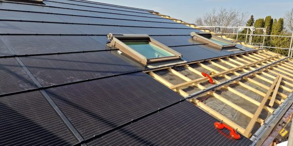 Dach mit Solarzelleninstallation und neuen Dachfenstern, Holzrahmen und Baustellenausrüstung sichtbar, unter blauem Himmel.